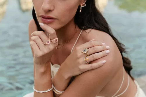 Woman wearing a white dress with two rings in both hands against a lake in the background.